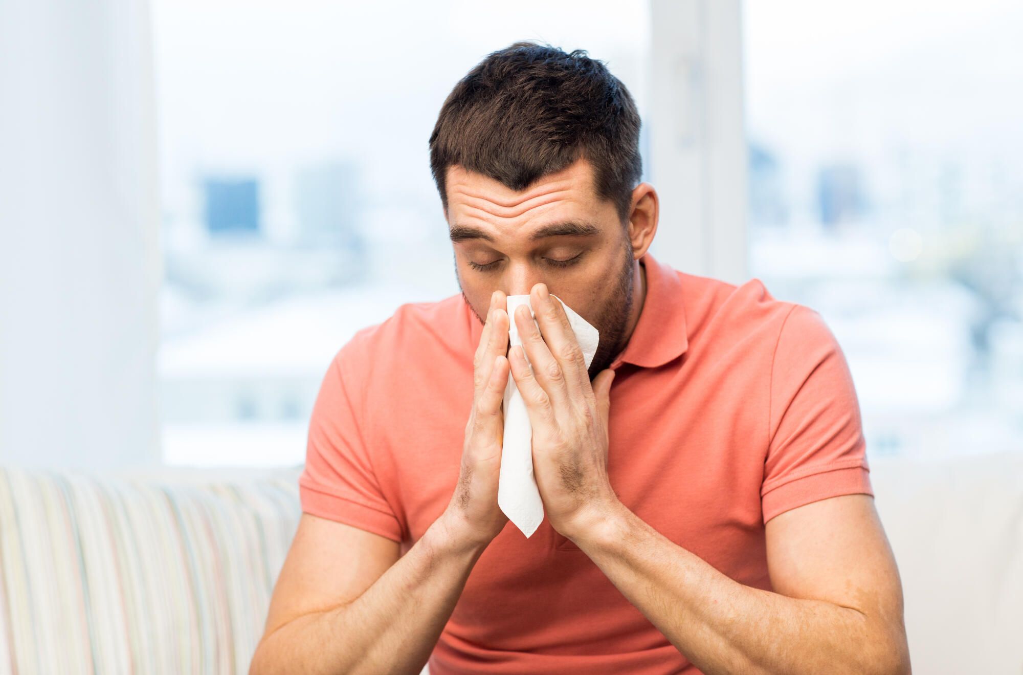 Man sneezing with a tissue indoors due to an allergy.