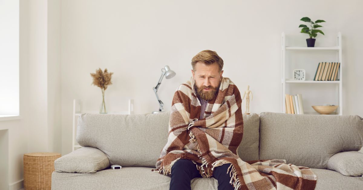 Man feeling cold, wrapped in a blanket indoors