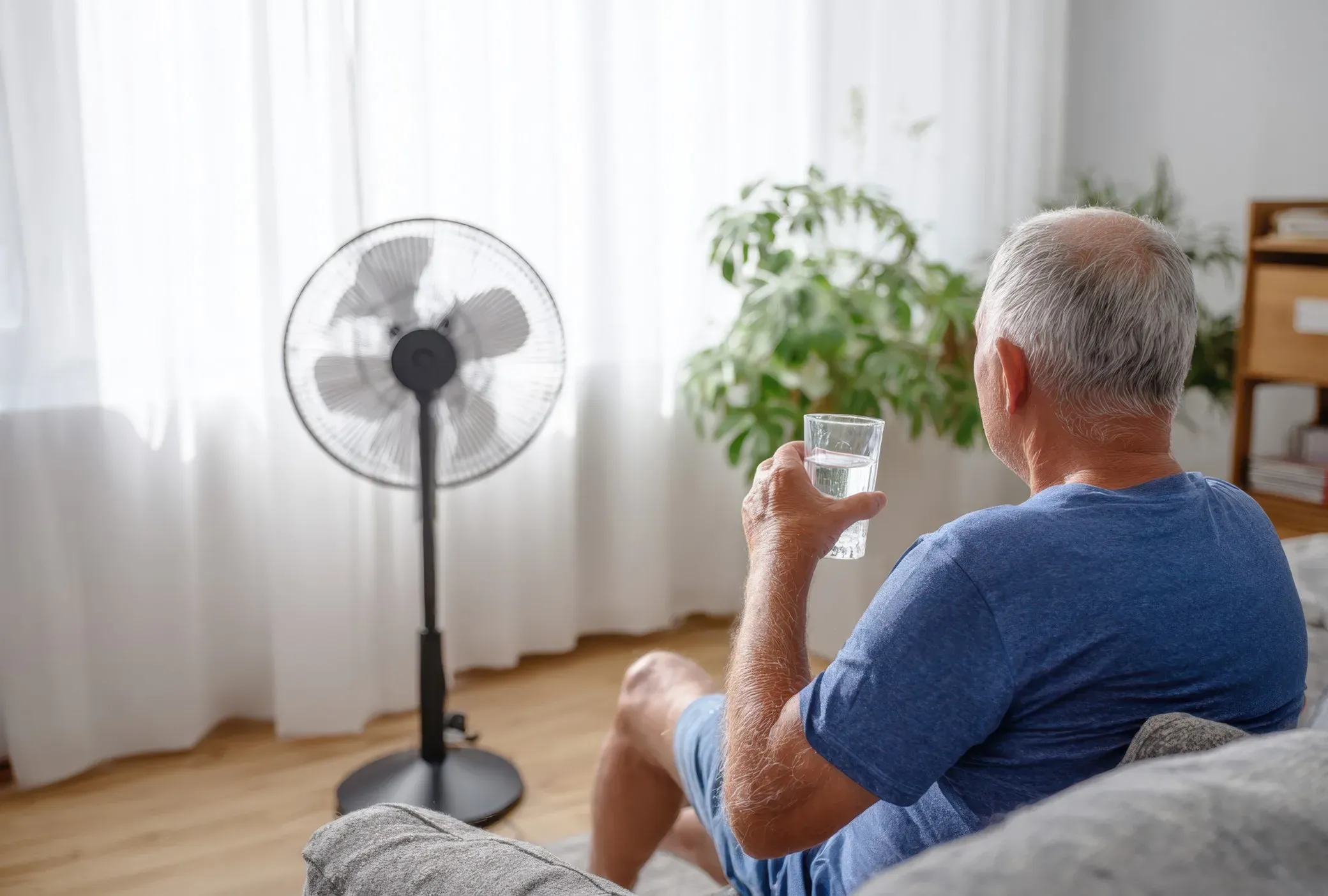 Senior man on couch with water and fan nearby